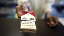 A "Smoking Kills" logo sits on a packet of Marlboro cigarettes, produced by Philip Morris International Inc., a unit of Altria Inc., as a shopkeeper holds the cigarette box over the counter in this arranged photograph taken behind a newsagent's counter in London, U.K., in London, U.K., on Friday, March 13, 2015. The U.K.'s unelected upper chamber, the House of Lords, is due to vote Monday on a standardized tobacco packaging legislation, after lawmakers in the lower chamber, the House of Commons, backed the plan. Photographer: Simon Dawson/Bloomberg via Getty Images
