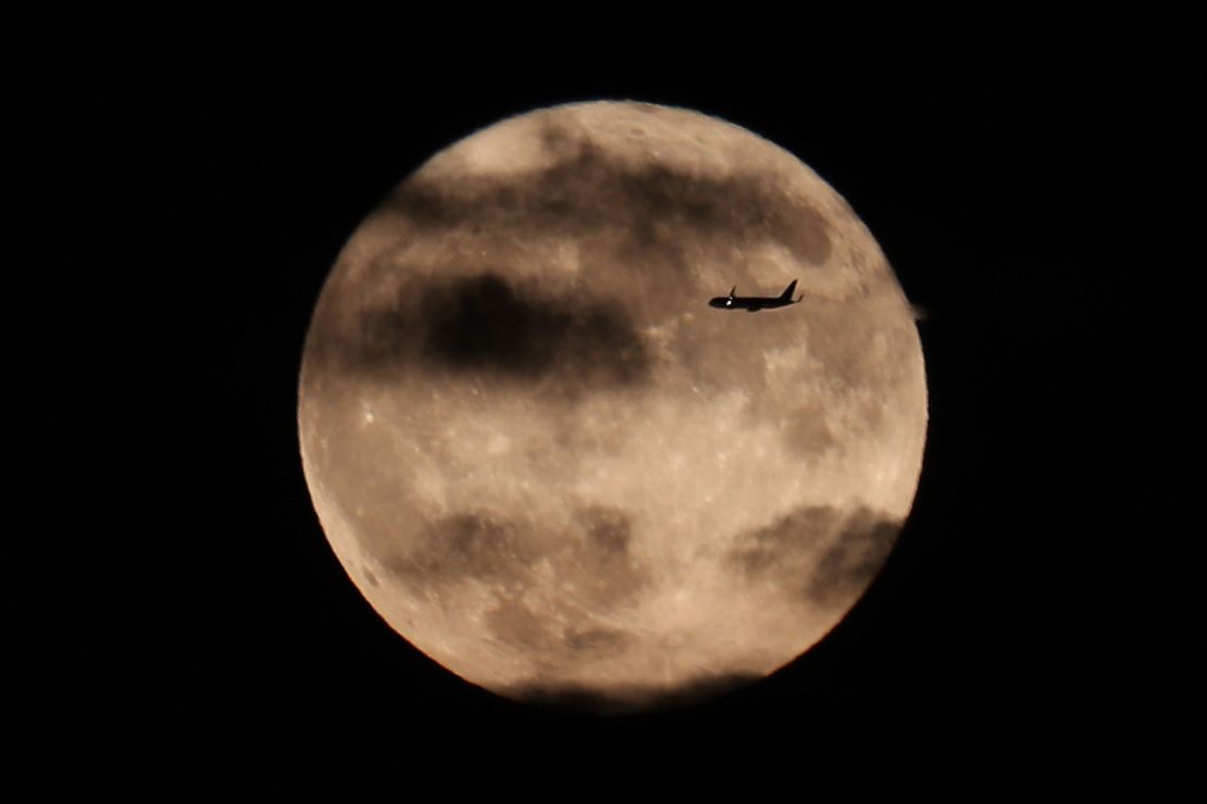 A plane flies past the harvest moon as it rises behind the Statue of Liberty in New York City, October 1, 2020.