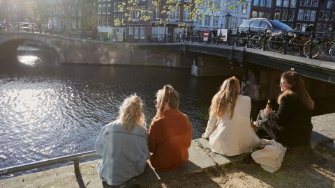 Some folks sit in the sun on a canal in Amsterdam. The Dutch treasure their niksen — or do nothing time.