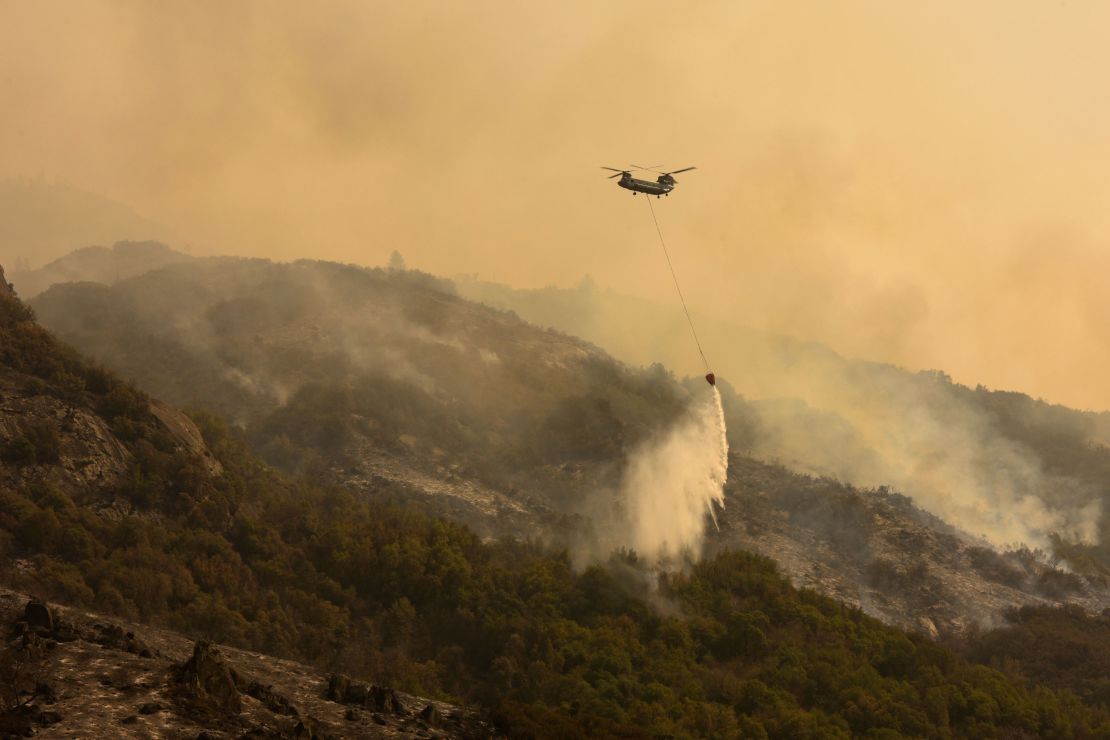 A Boeing CH-47 Chinook firefighting helicopter carries water to drop on the fire as smoke rises in the foothills along Generals Highway during a media tour of the KNP Complex fire in the Sequoia National Park near Three Rivers, California on September 18, 2021.
