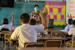 Students and their teacher wear protective face masks in their elementary school.