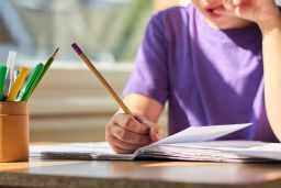 A young child sits at a classroom table  completing school work.