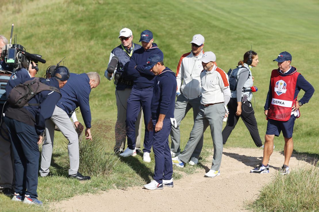 A rules offical inspects the lie of a ball for Berger and Koepka on the 15th hole.