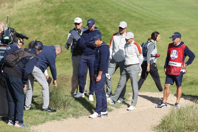 An official inspects the lie of a ball for Team US' Brooks Koepka (center) and Daniel Berger on the 15th hole. The pair <a href="index.php?page=&url=https%3A%2F%2Fwww.cnn.com%2F2021%2F09%2F25%2Fgolf%2Fbrooks-koepka-drop-controversy-ryder-cup-spt-intl%2Findex.html" target="_blank">called over two sets of officials</a> to attempt to get a free drop but it was ultimately refused.