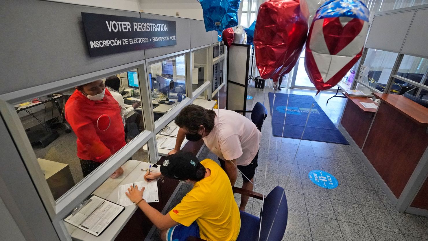 Lucas Saez, foreground, 22, fills out his voter registration form as his father Ramiro Saez, center rear, looks on, Tuesday, Oct. 6, 2020, at the Miami-Dade County Elections Department in Doral, Fla. 