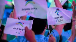 Participants wave flags with the logos of 2022 Beijing Winter Olympics and Paralympics before a launch ceremony to reveal the motto for the Winter Olympics and Paralympics in Beijing, Friday, Sept. 17, 2021. Organizers on Friday announced "Together for a Shared Future" as the motto of the next Olympics, which is scheduled to begin on Feb. 4 of next year. (AP Photo/Mark Schiefelbein)