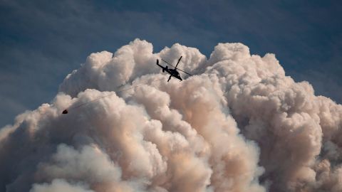 A helicopter carrying a water bucket flies past a pyrocumulus cloud produced by a wildfire burning in the mountains above Lytton, British Columbia, in August.