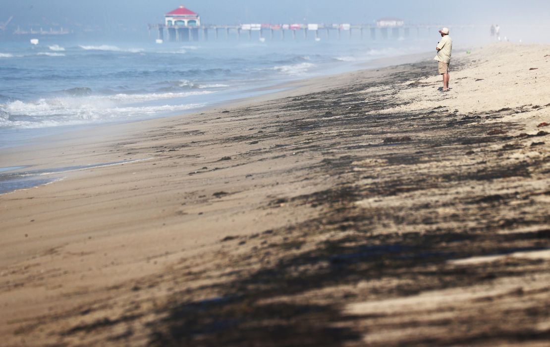 A person stands Sunday near oil washed up on Huntington State Beach in California.