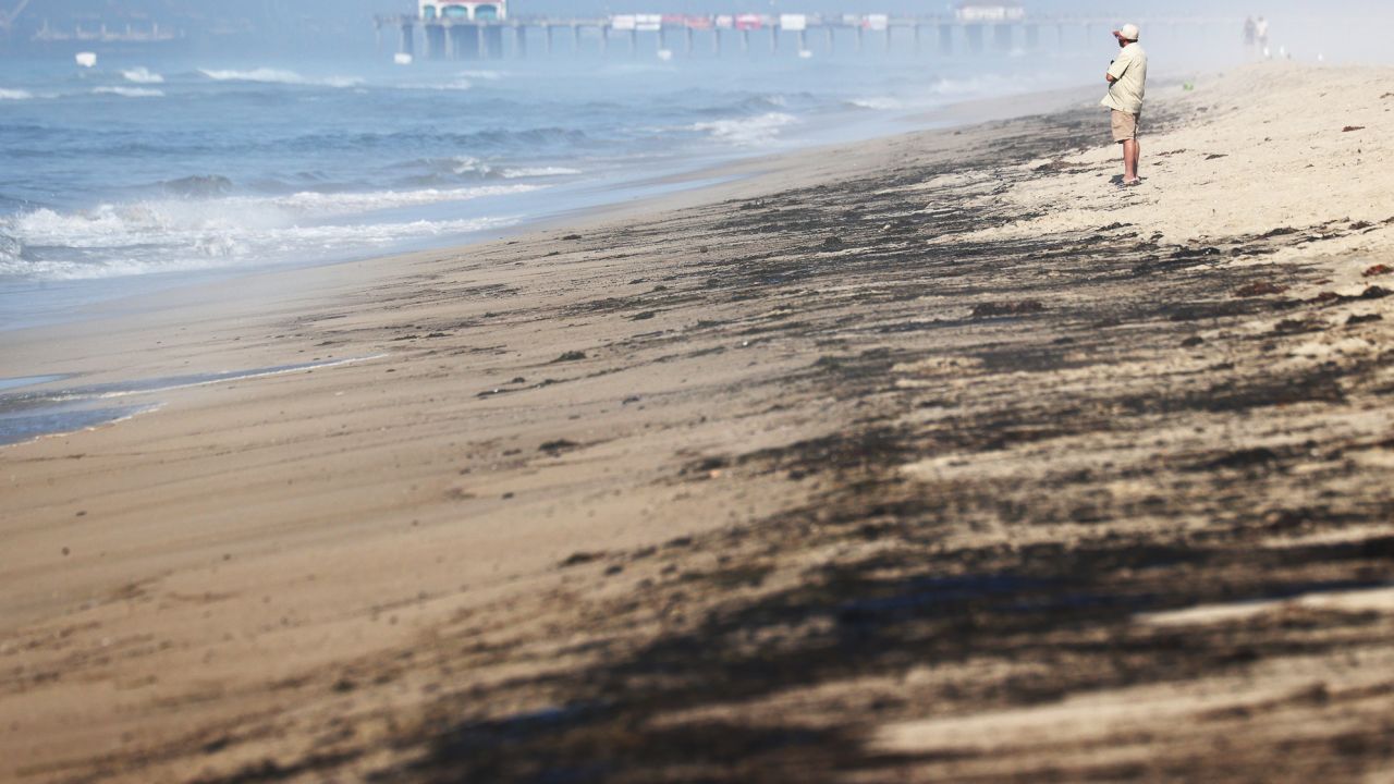 A person stands Sunday near oil washed up on Huntington State Beach in California.