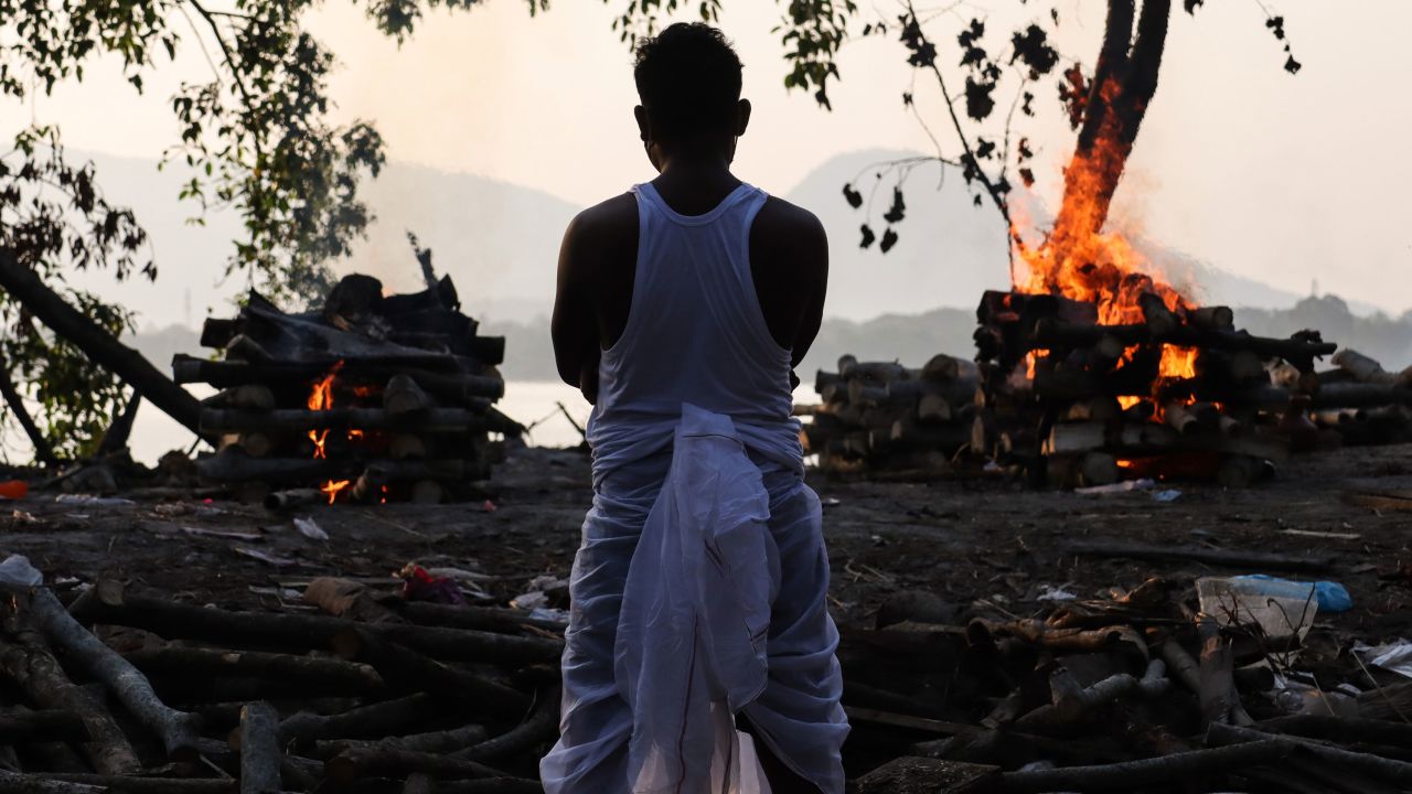 A family member standing next to the cremation of a coronavirus victim, on the banks of Brahmaputra River, in Guwahati, Assam, India in May 2021.