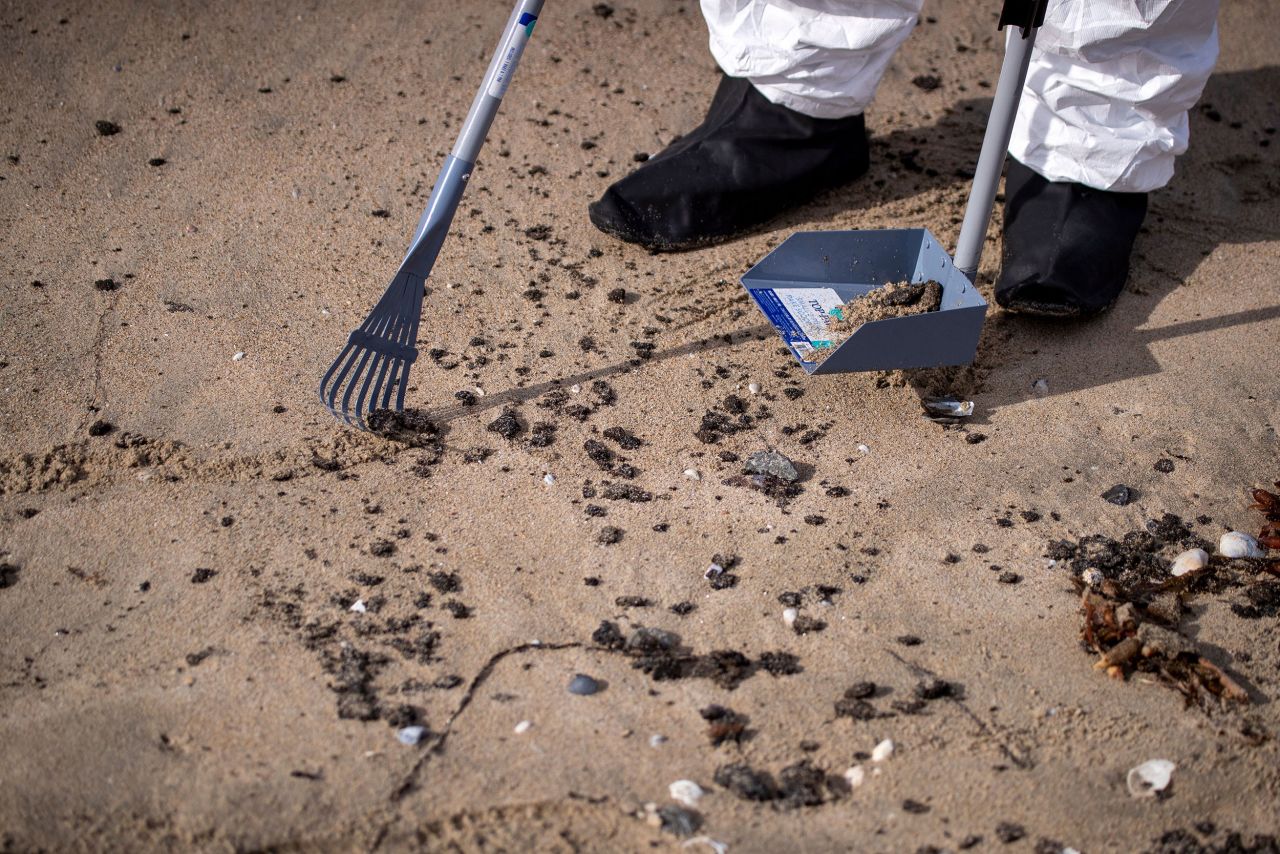 A member of a cleanup crew rakes up some of the oil that washed ashore on Huntington Beach.
