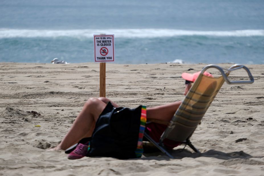 A beachgoer sits in front of a warning sign in Huntington Beach on October 4.