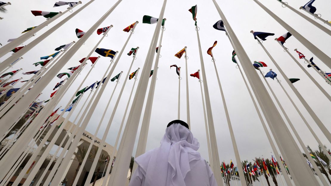 An Emirati visitor stands beneath the waving flags of countries participating in the Expo 2020 in the Gulf Emirate of Dubai on October 6, 2021.