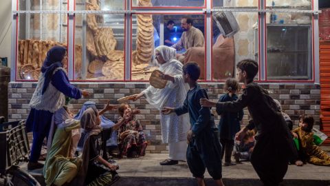 A woman gives bread to young people in need in front of bakery in Kabul on September 19, 2021.