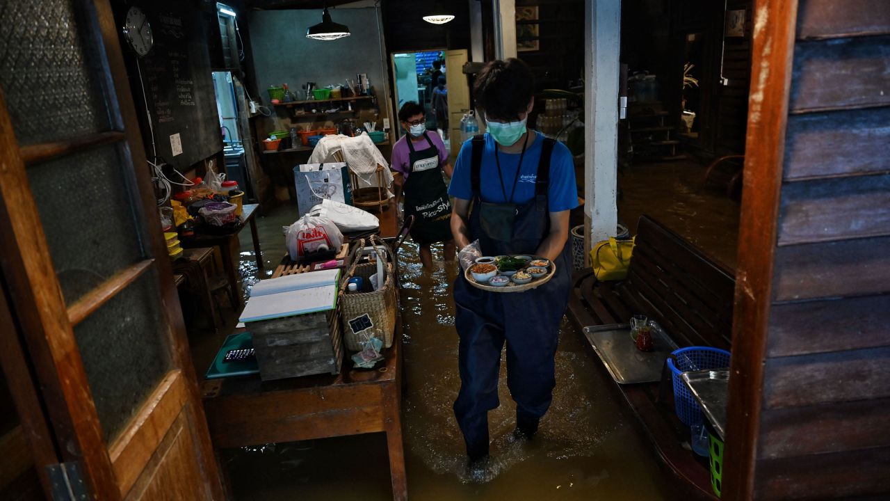This photo taken on October 7, 2021, shows an employee serving food at the Chaopraya Antique Cafe, as flood water from the Chao Phraya River surges into the restaurant, in Nonthaburi province north of Bangkok. (Photo by Lillian SUWANRUMPHA / AFP) (Photo by LILLIAN SUWANRUMPHA/AFP via Getty Images)