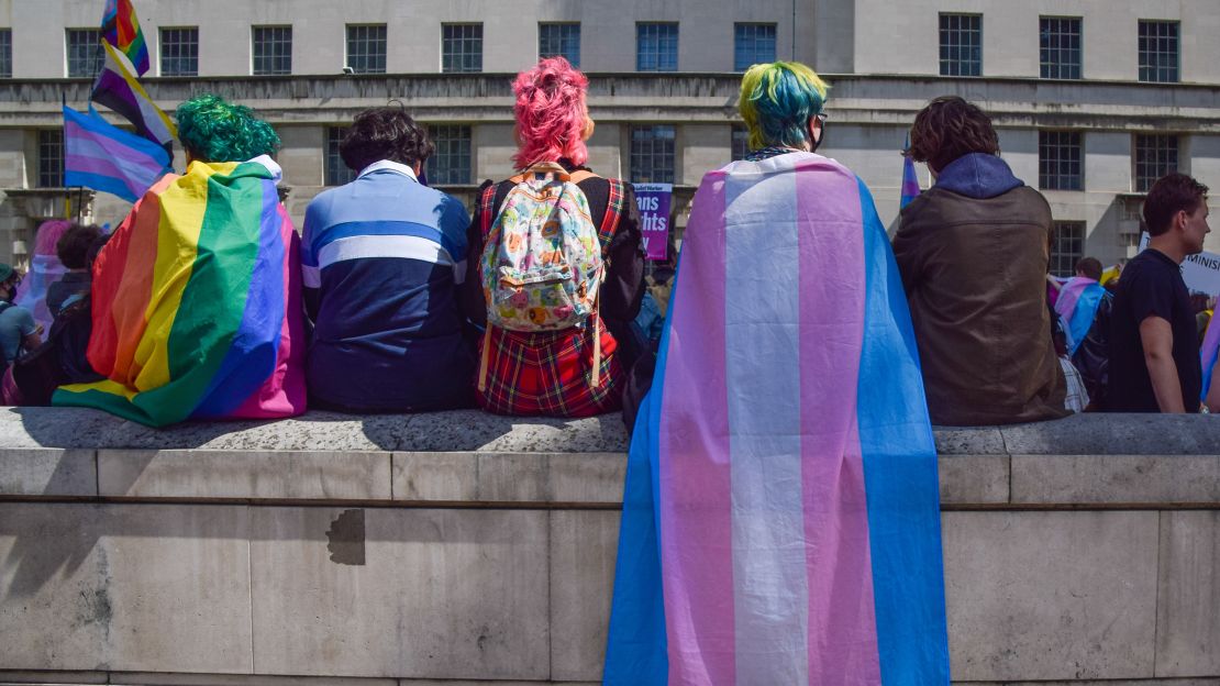 Protesters wrapped in pride and trans pride flags sit on a wall during a trans rights demonstration outside Downing Street.