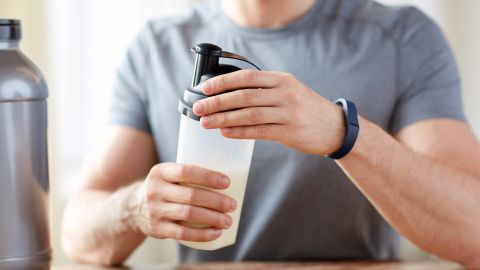A man wearing a fitness tracker prepares a protein shake.