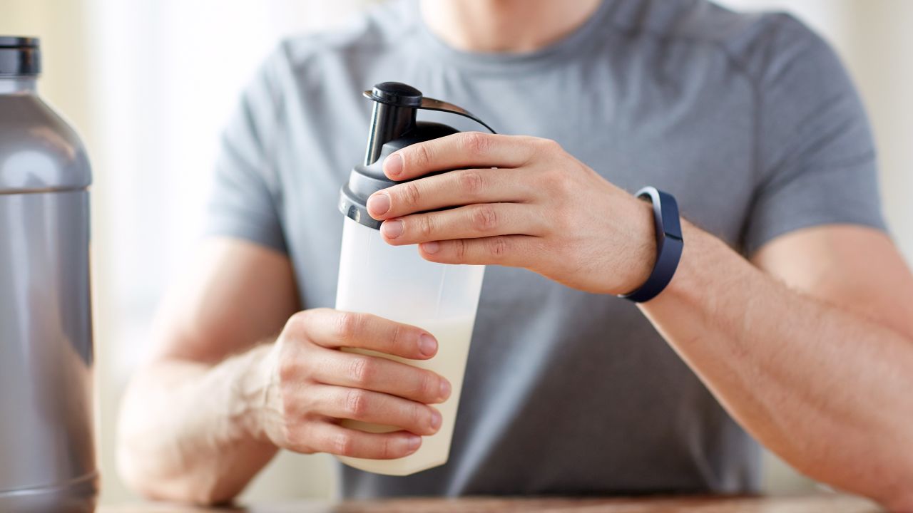 A man wearing a fitness tracker prepares a protein shake.