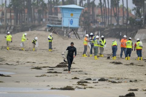 A surfer leaves the water as workers continue cleanup efforts in Huntington Beach, California, on Monday, October 11. Huntington Beach had just reopened its shoreline.