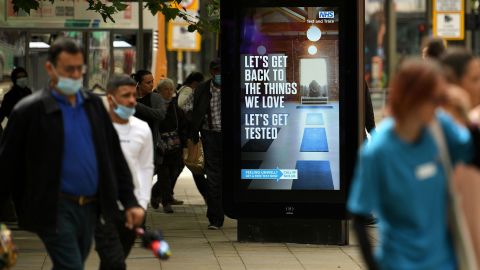 Pedestrians walk past an electronic display board promoting the "Test and Trace" coronavirus tracking scheme in Manchester, England, on August 3, 2020.