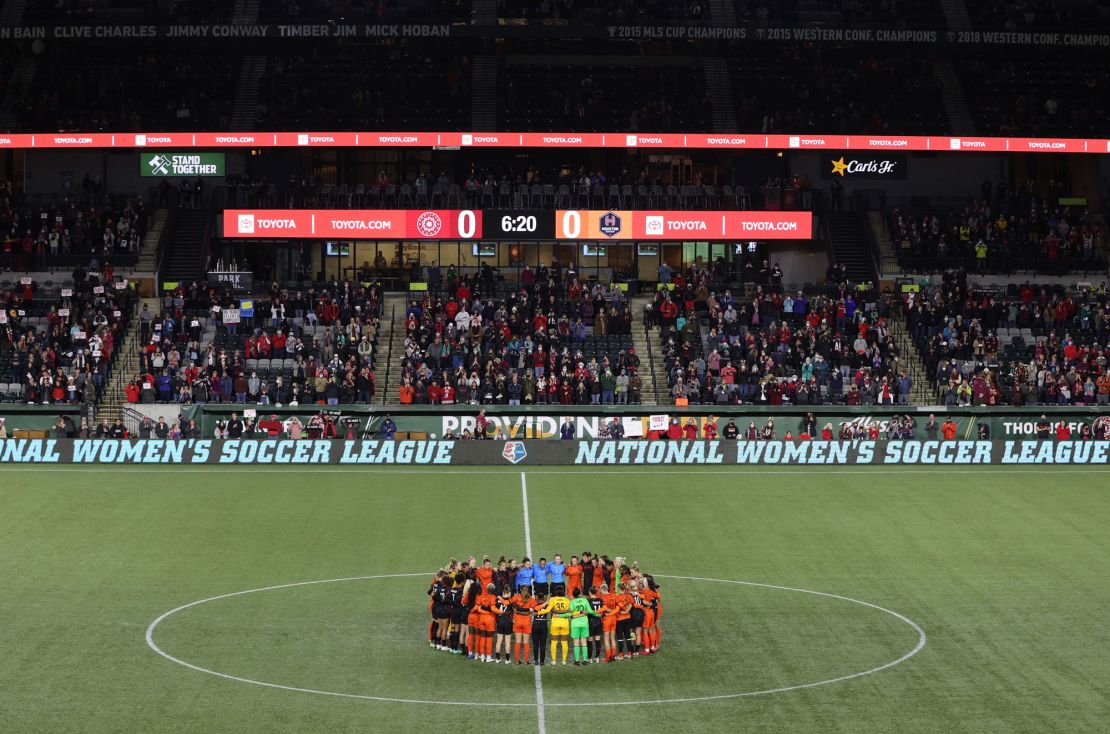 Portland Thorns and Houston Dash players, along with referees, gather at midfield in demonstration of solidarity.