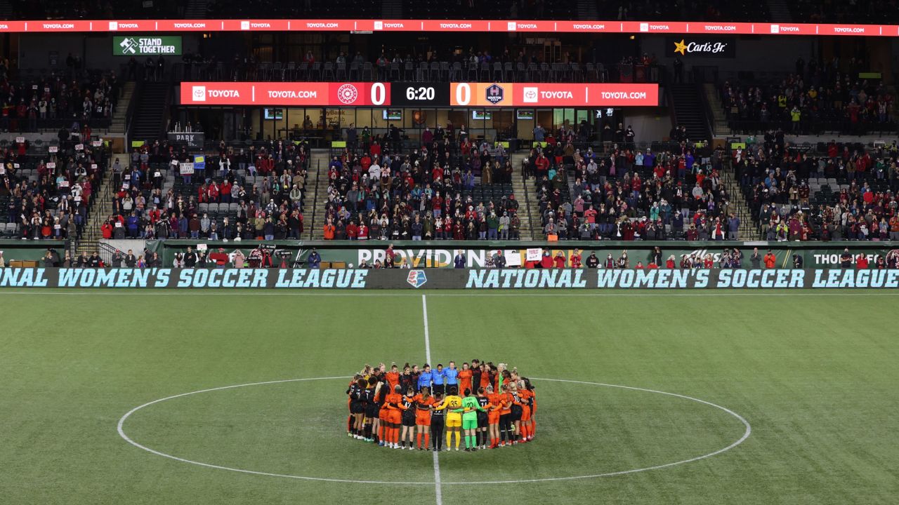 Portland Thorns and Houston Dash players, along with referees, gather at midfield in demonstration of solidarity.