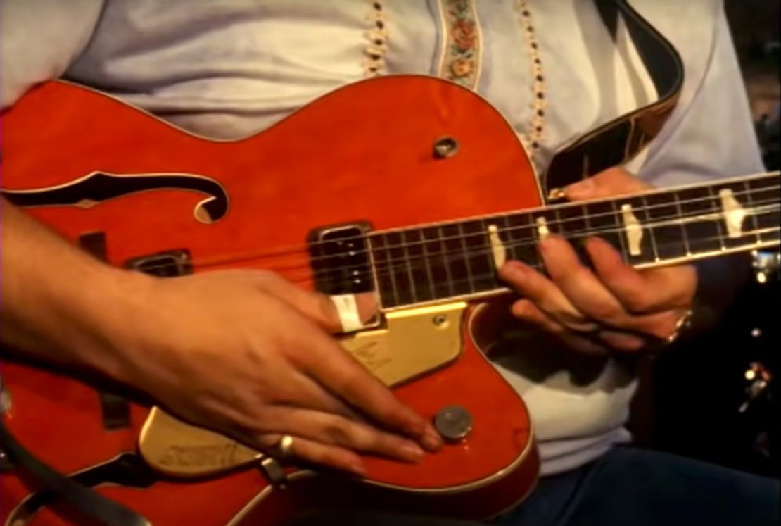 A close up of Randy Bachman's guitar shows a dime-sized ring near the knob he's adjusting.