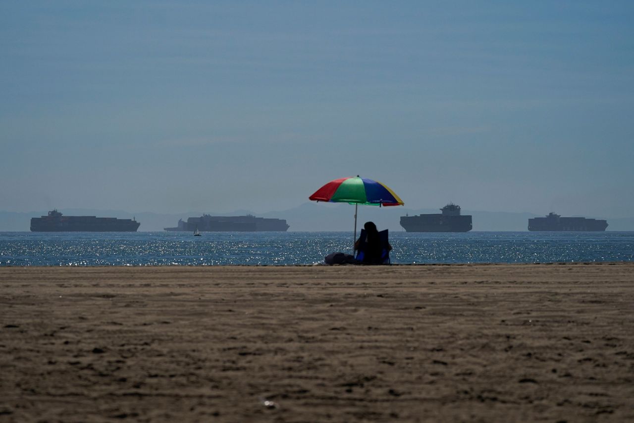 A person sits on the beach in Seal Beach, California, on October 1 as container ships wait to dock at the Ports of Los Angeles and Long Beach.