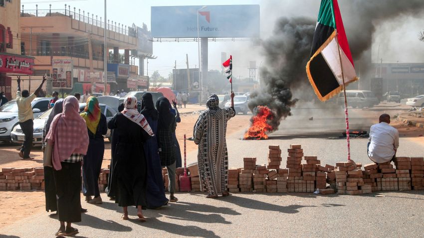 Sudanese protesters lift national flags next to a brick roadblock during a demonstration in the capital Khartoum, on October 25, 2021, to denounce overnight detentions by the army of members of Sudan's government. - Armed forces detained Sudan's Prime Minister over his refusal to support their "coup", the information ministry said, after weeks of tensions between military and civilian figures who shared power since the ouster of autocrat Omar al-Bashir. (Photo by AFP) (Photo by -/AFP via Getty Images)