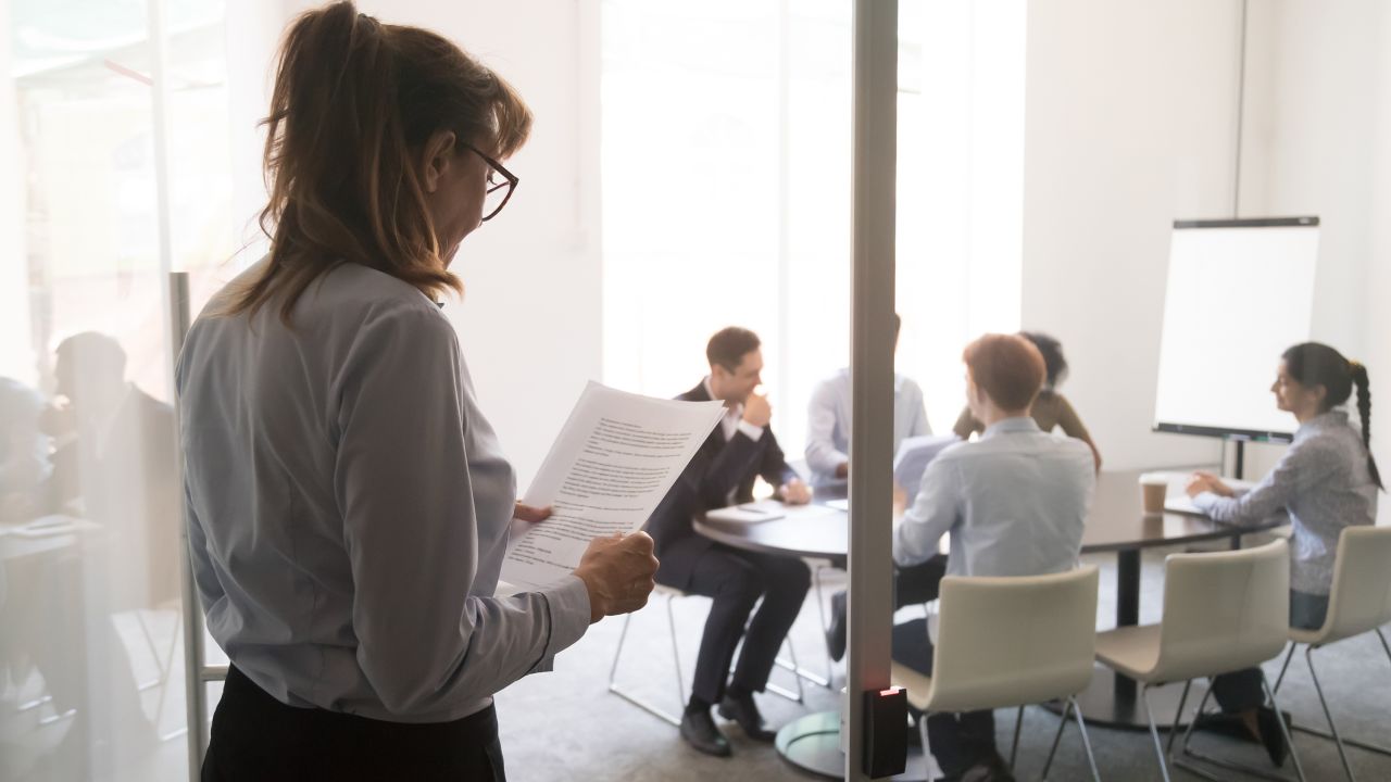 A businesswoman stands at an office door, feeling nervous before her presentation for a meeting.