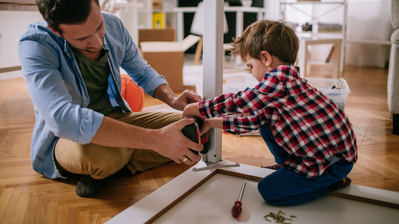 Little boy is trying to assemble the furniture with a little help from his father, in their living room 