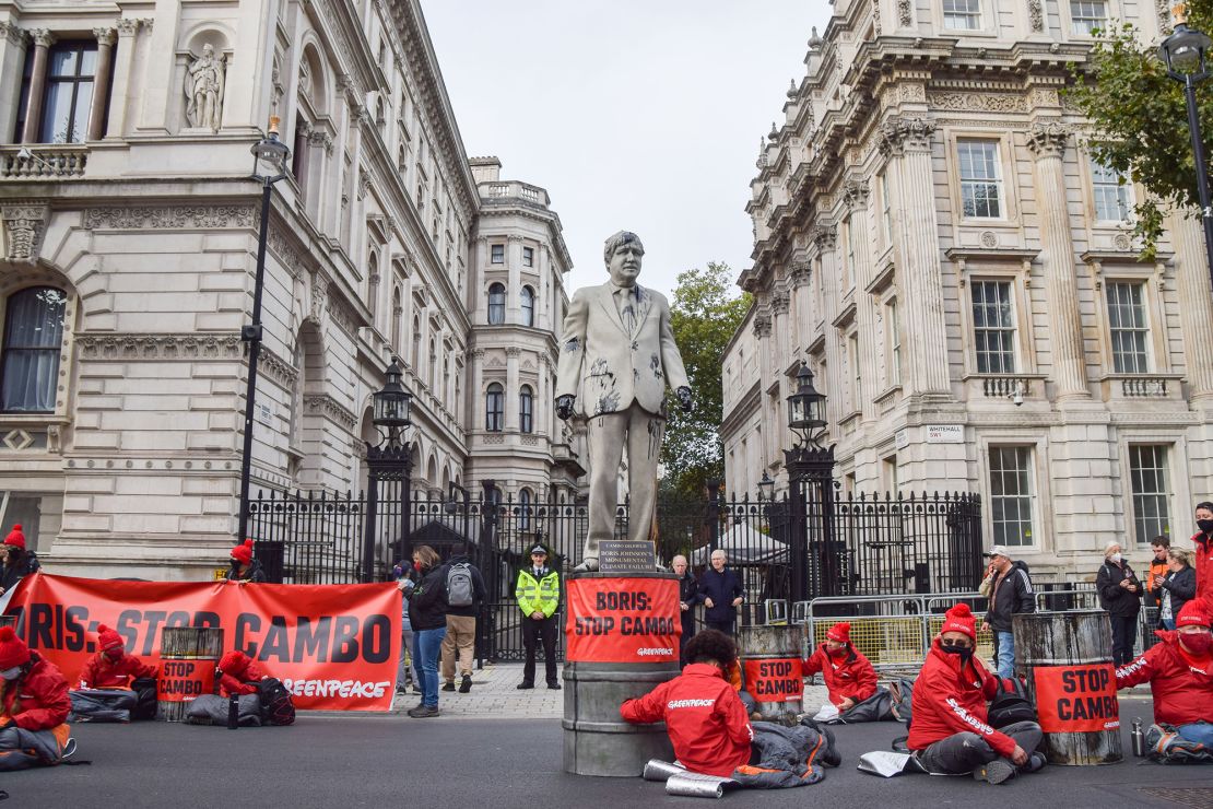 Activists locked to barrels sit around a statue of Prime Minister Boris Johnson splattered with fake oil during a protest of the development of the Cambo oilfield.