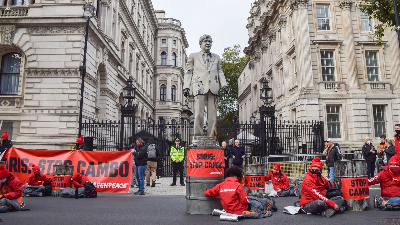 Activists locked to barrels sit around a statue of Prime Minister Boris Johnson splattered with fake oil during a protest of the development of the Cambo oilfield.