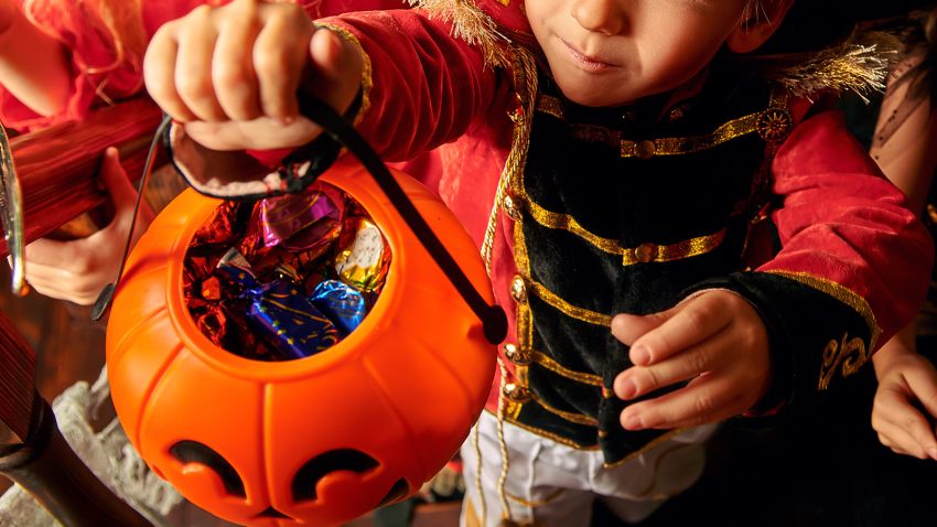 Happy children in carnival costumes trick or treating with pumpkin basket in the old wooden house. Halloween party. 