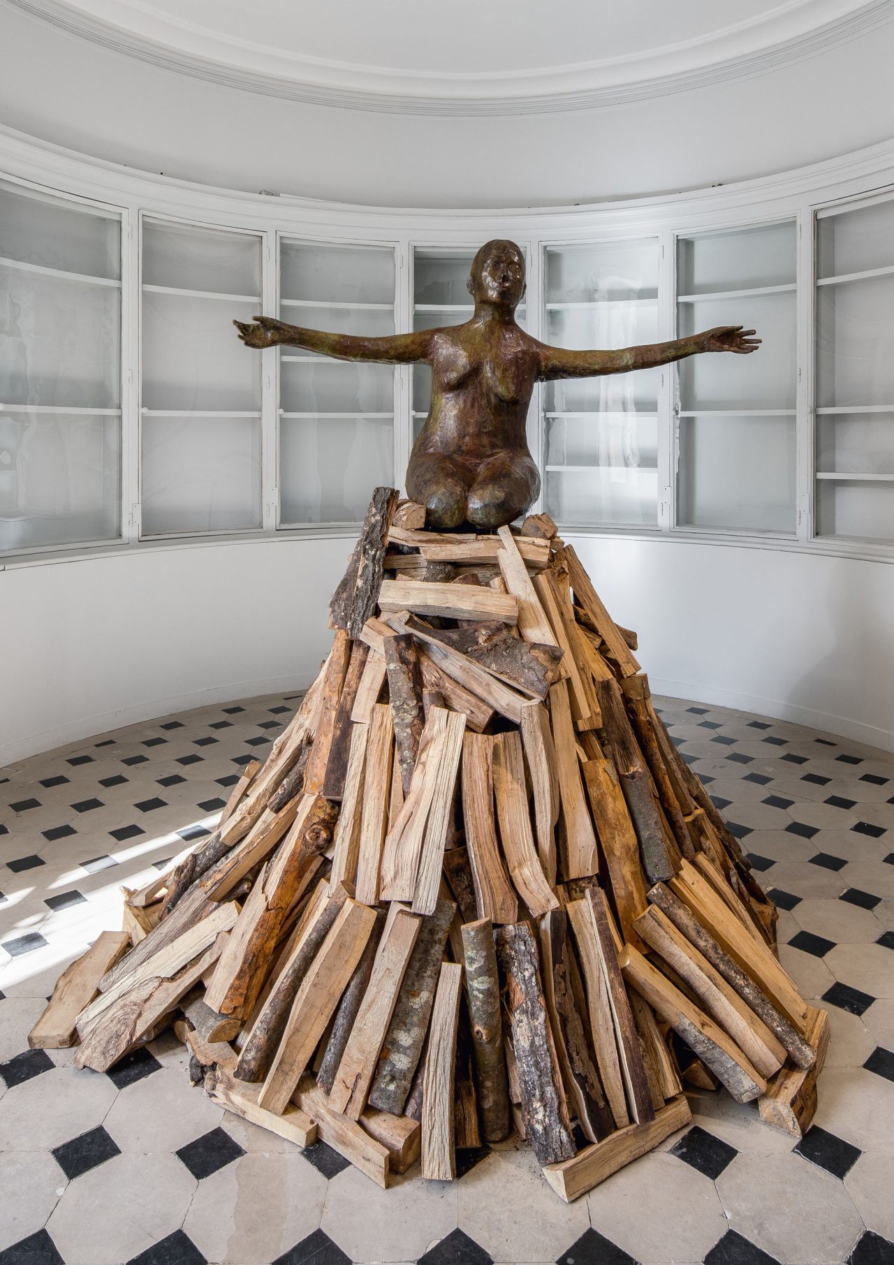 In Kiki Smith's work "Pyre Woman Kneeling," a bronze female figure tops a pyre. The statue commemorates women who were burned for witchcraft.