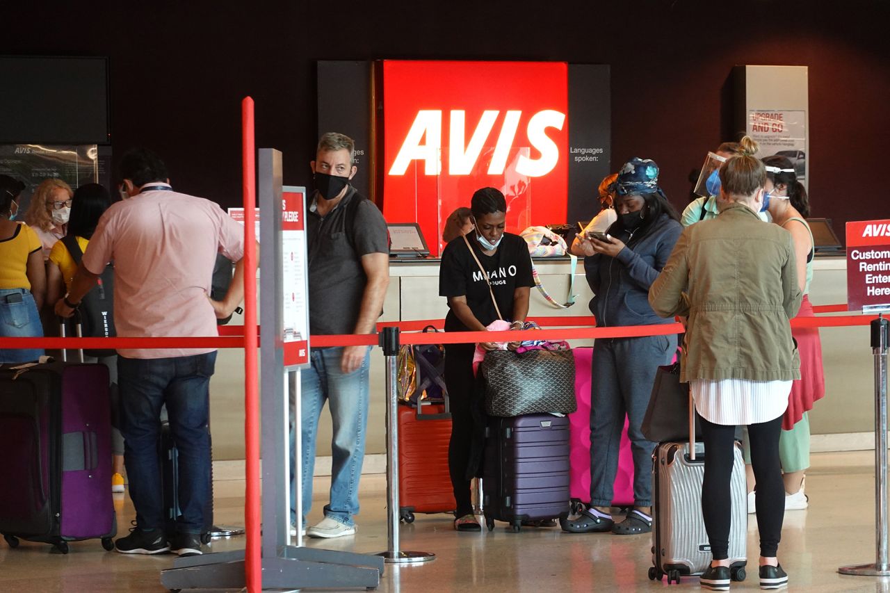 People wait in line to get a vehicle at the Avis desk at Miami International Airport Car Rental Center on April 12, 2021. Travelers might find long waits and sky-high prices this year, too.