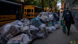 Pedestrians pass by trash bags piled on a street in Manhattan following a slow down in garbage collection by workers unhappy with mandatory vaccinations imposed by Mayor Bill de Blasio, in New York on October 28, 2021. (Photo by Ed JONES / AFP) (Photo by ED JONES/AFP via Getty Images)