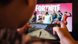 August 15, 2020, Makassar, South Sulawesi, Indonesia: A child is playing a game on a cellphone with a picture of the Fortnite game on the computer screen in the background. Apple and Google announced their decision to remove Fortnite games from the App Store and Google Play app stores. (Credit Image: © Herwin Bahar/ZUMA Wire)