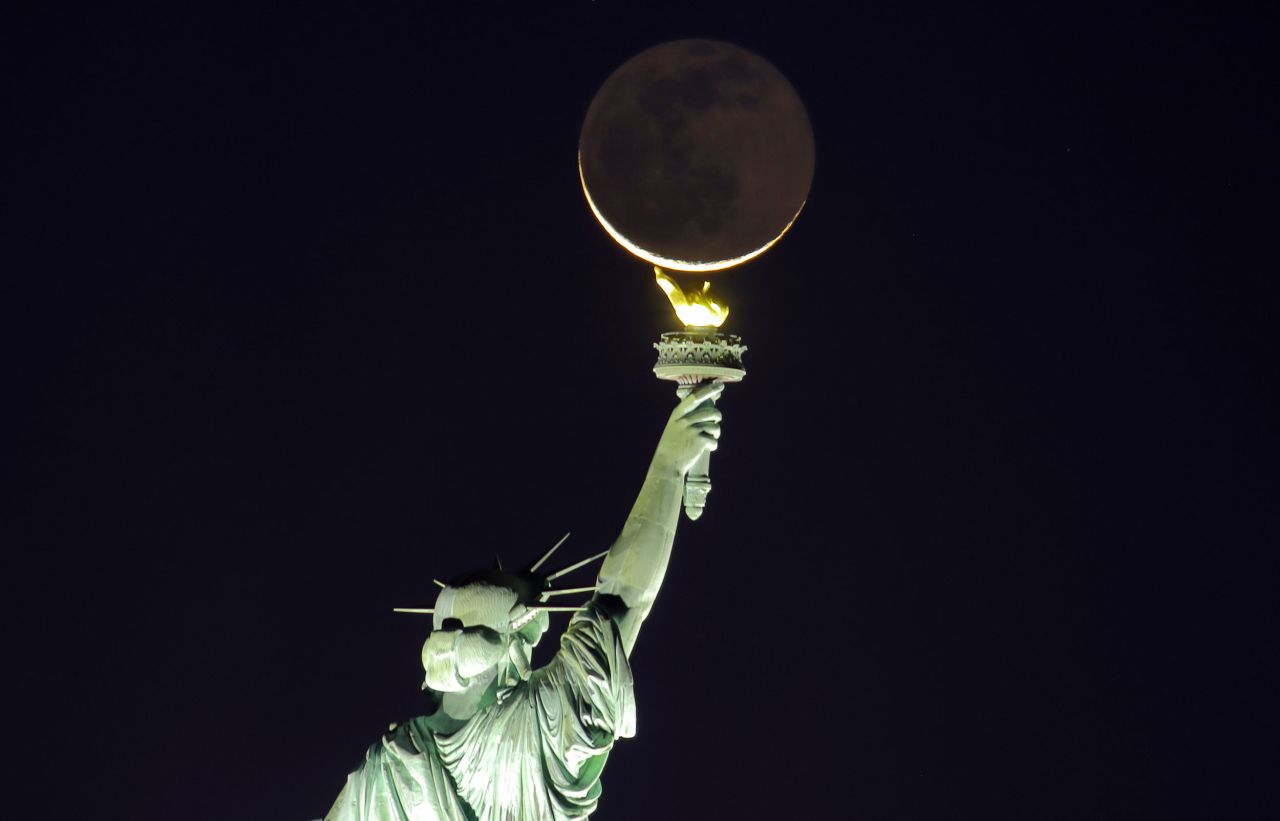 The moon, seen from Jersey City, New Jersey, rises behind the Statue of Liberty in New York before sunrise on Wednesday, November 3.