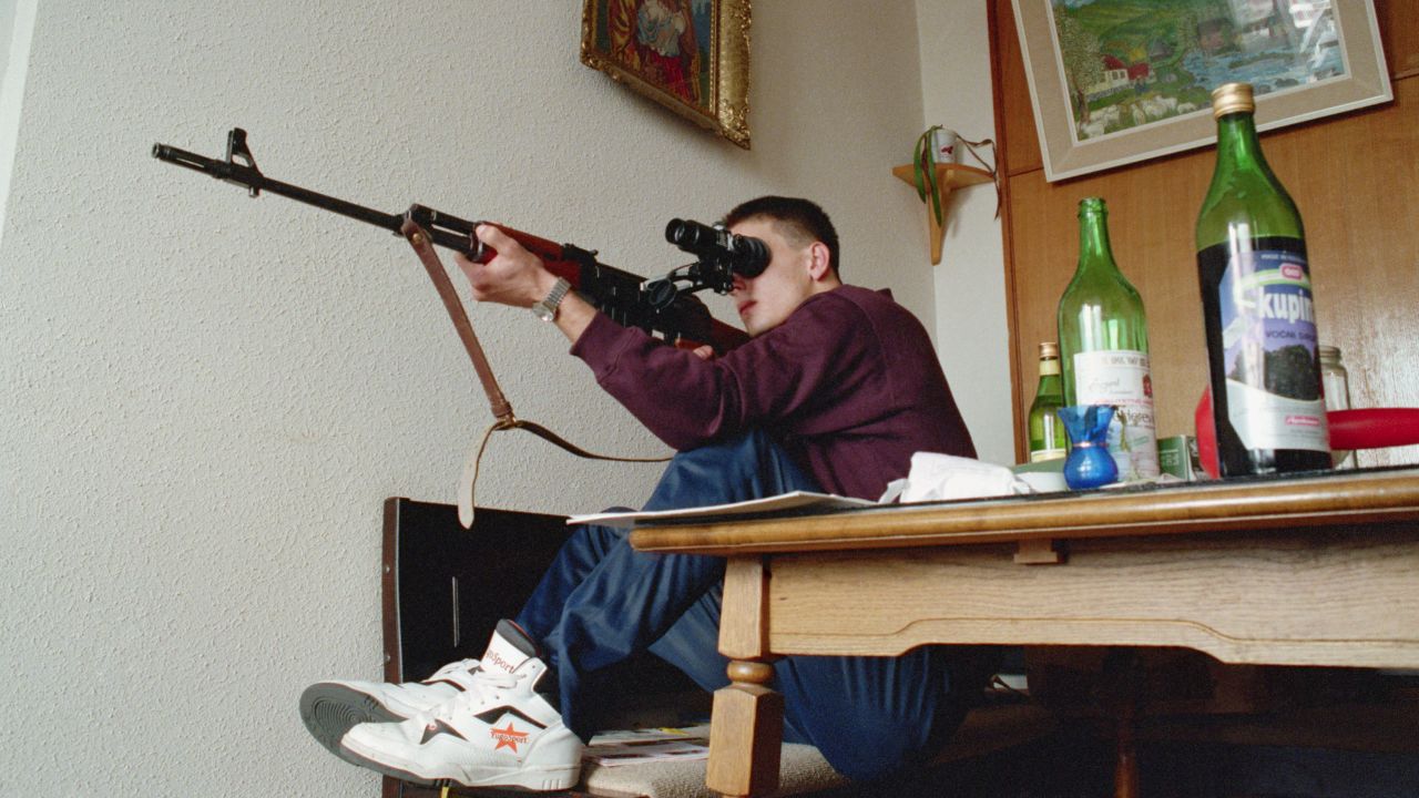 A Bosnian sniper attempts to shoot Serbian snipers in the mountains from his position on the 20th floor of a Sarajevo building during the war in the 1990s.