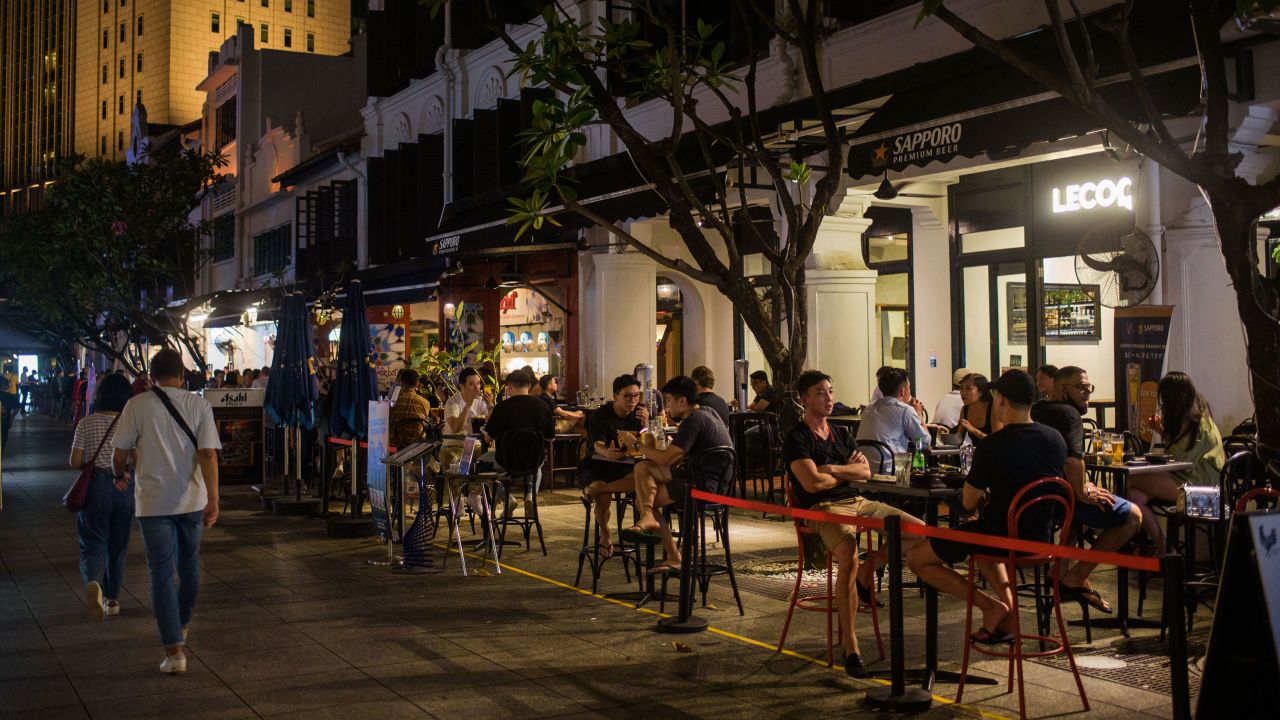 People seated at tables in groups of two as mandated by Covid-19 safety restrictions drink at bars in Singapore on October 23, 2021.