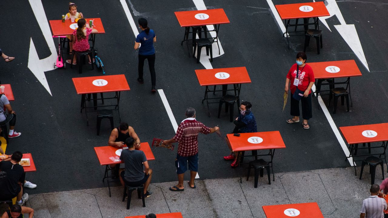 People seated in groups of two as mandated by Covid-19 restrictions are served by staff at a food center  in Singapore on October 23 2021.