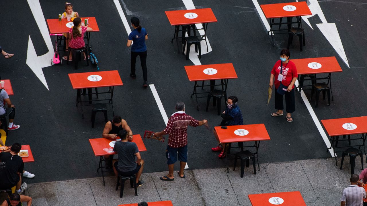 People seated in groups of two as mandated by Covid-19 restrictions are served by staff at a food center in Singapore on October 23 2021.