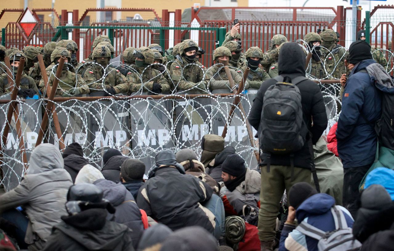 Migrants sit in front of Polish troops at the border crossing on Monday, November 15.
