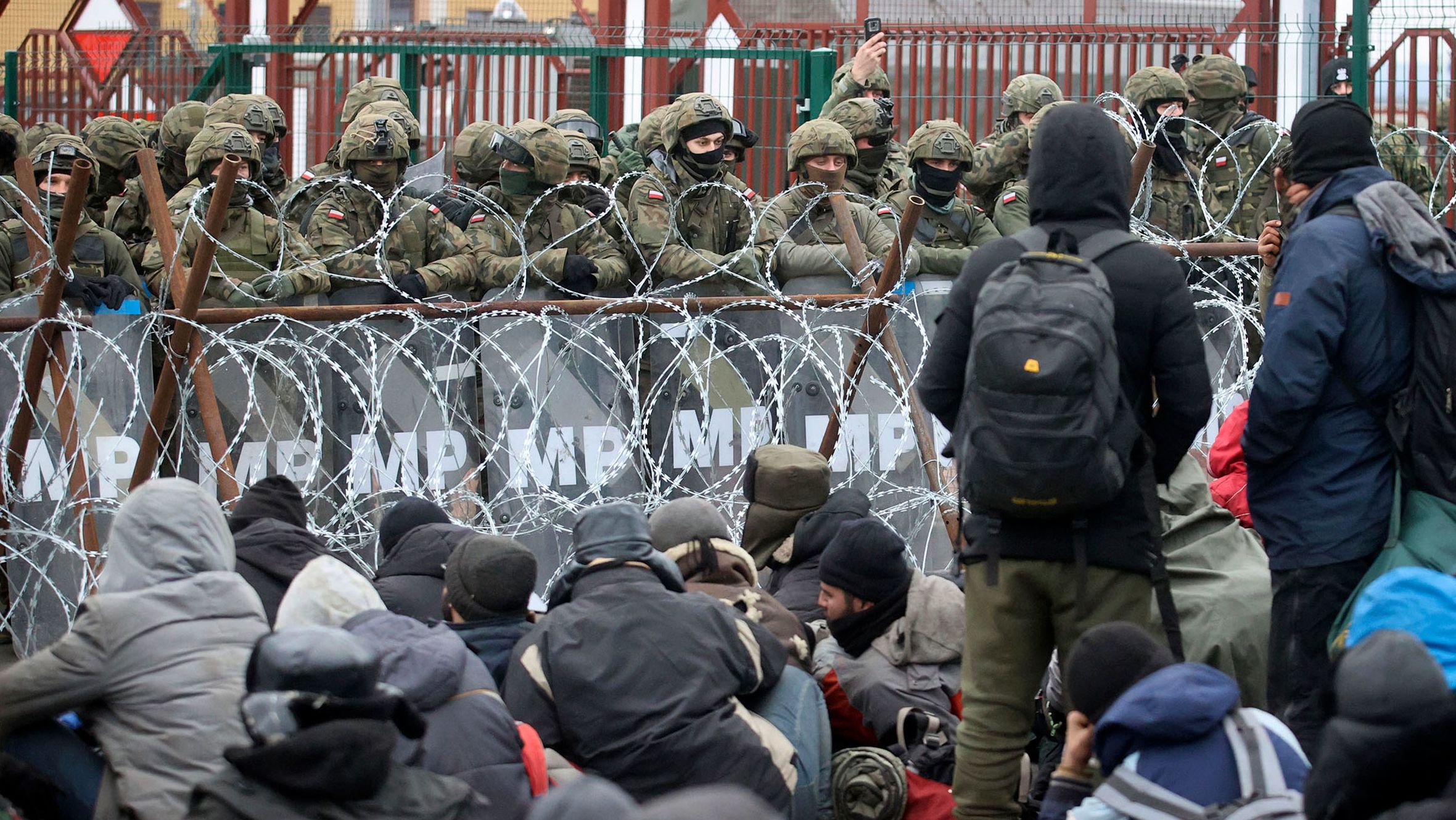 Migrants sit in front of Polish troops at the border crossing on Monday, November 15.