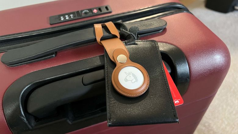 A photo of an Apple AirTag attached to a red suitcase