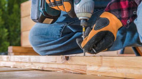Male Carpenter Using Cordless Drill To Drive Long Screw Through Wooden Planks.