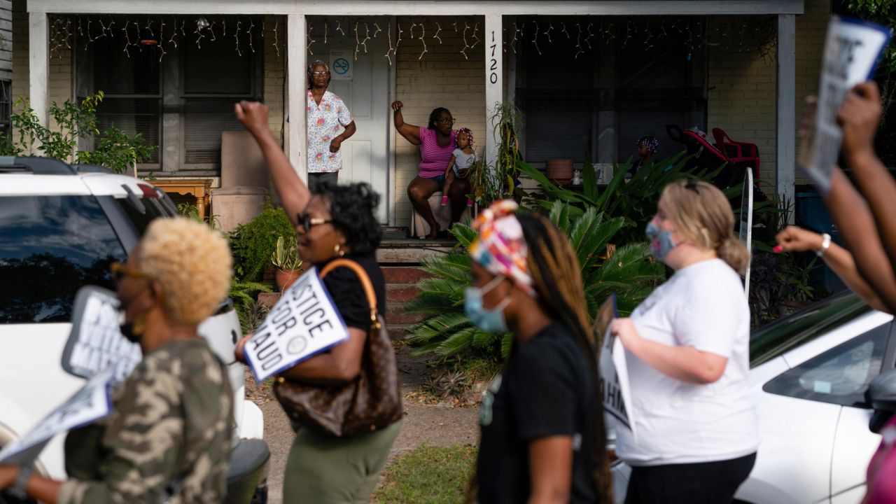 Sadie Rhone, standing at rear left, watches as marchers pass by her home in Brunswick.