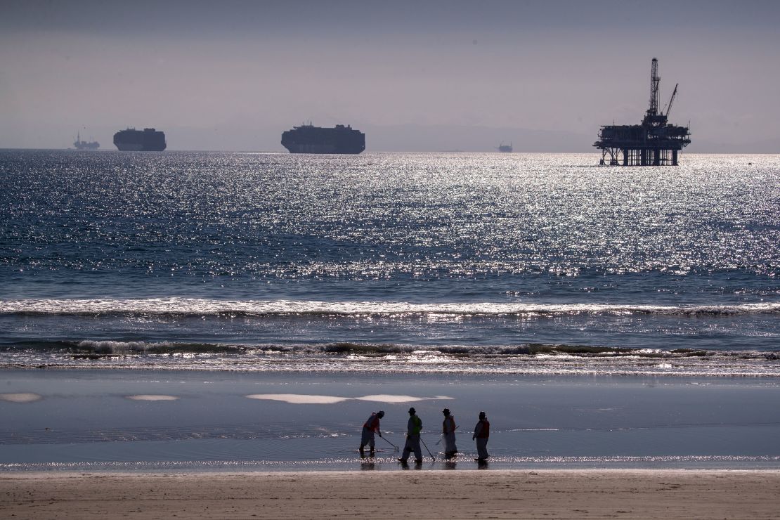 Container ships and an oil derrick line in the horizon as environmental oil spill cleanup crews search Huntington Beach on October 5, 2021, cleaning up oil chucks from the oil spill