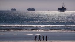 Container ships and an oil derrick line the horizon as environmental oil spill cleanup crews search the beach, cleaning up oil chucks from a major oil spill in Huntington Beach Tuesday, Oct. 5, 2021.